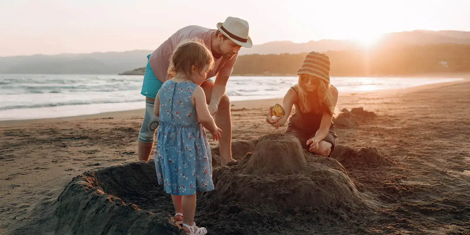 Une famille en vacances petit budget qui construit un château de sable sur la plage au coucher du soleil