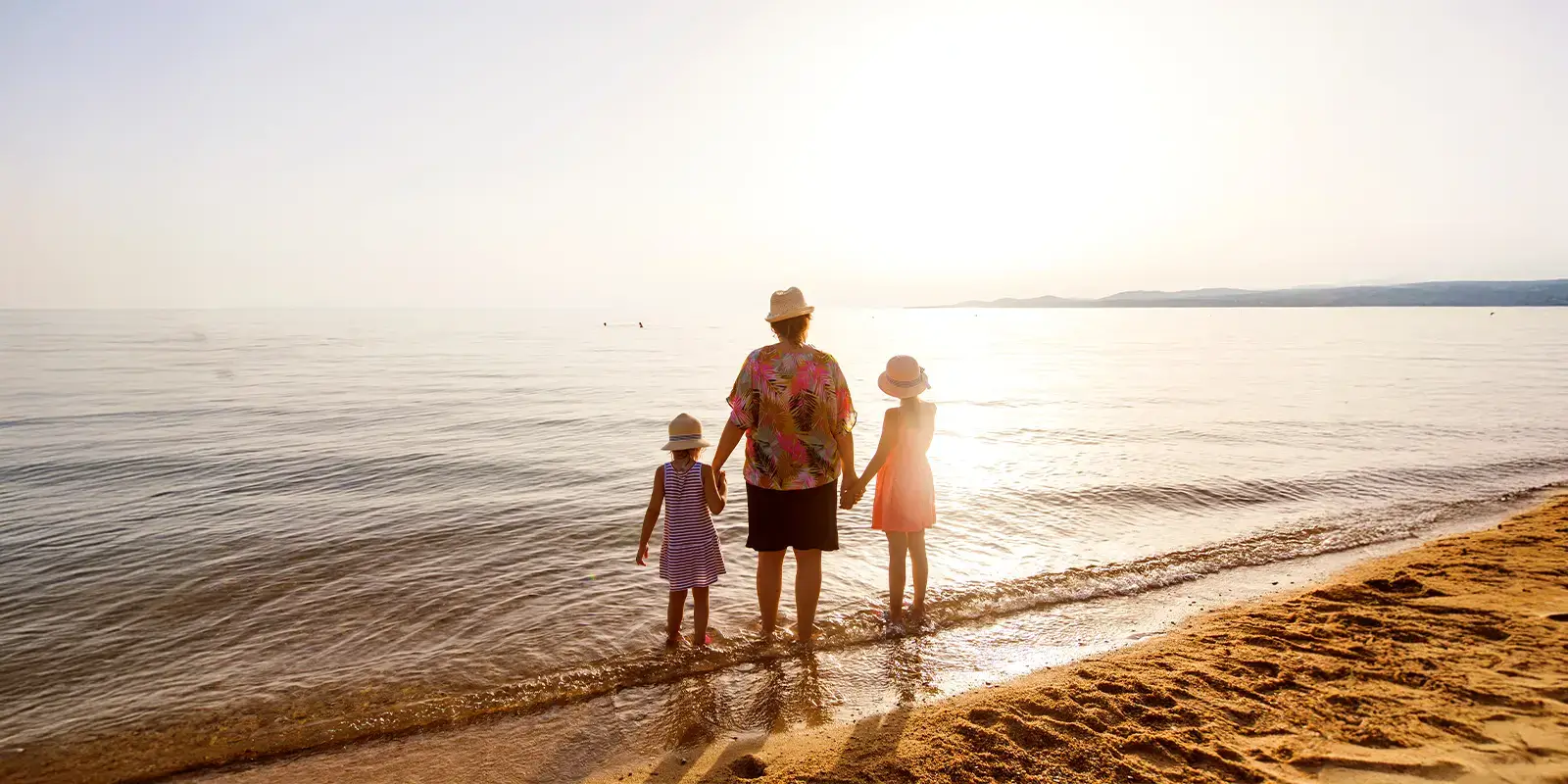 Une maman et ses deux filles profitant d'un coucher de soleil en bord de mer grâce aux aides VACAF
