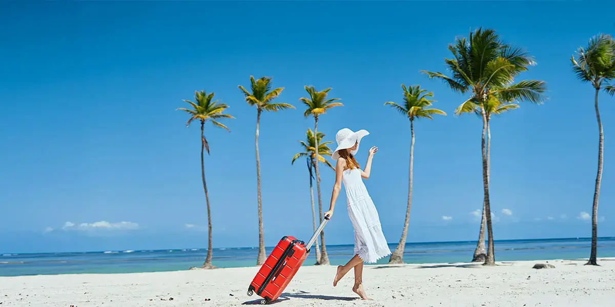 Jeune femme marche sur la plage avec sa valise de vacances