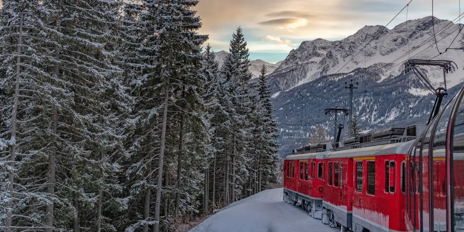Train rouge traversant une forêt enneigée au pied des montagnes