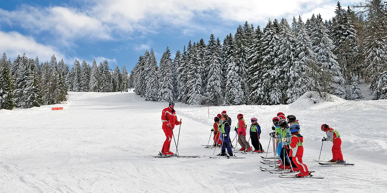 Moniteur et groupe d'enfants sur une piste bordée de sapins enneigés
