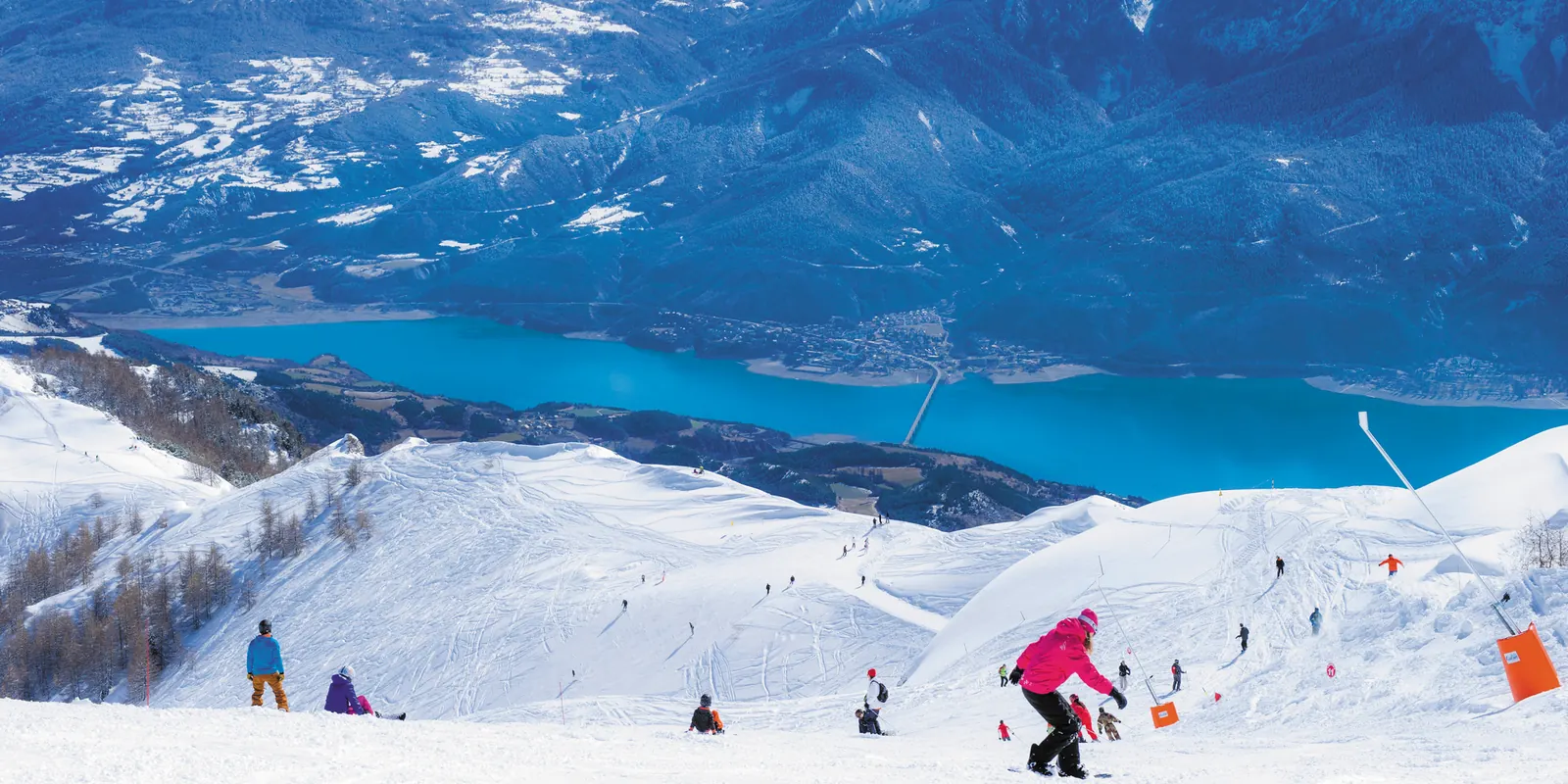 Skieurs sur les pistes de Réallon avec vue sur le lac de Serre-Ponçon
