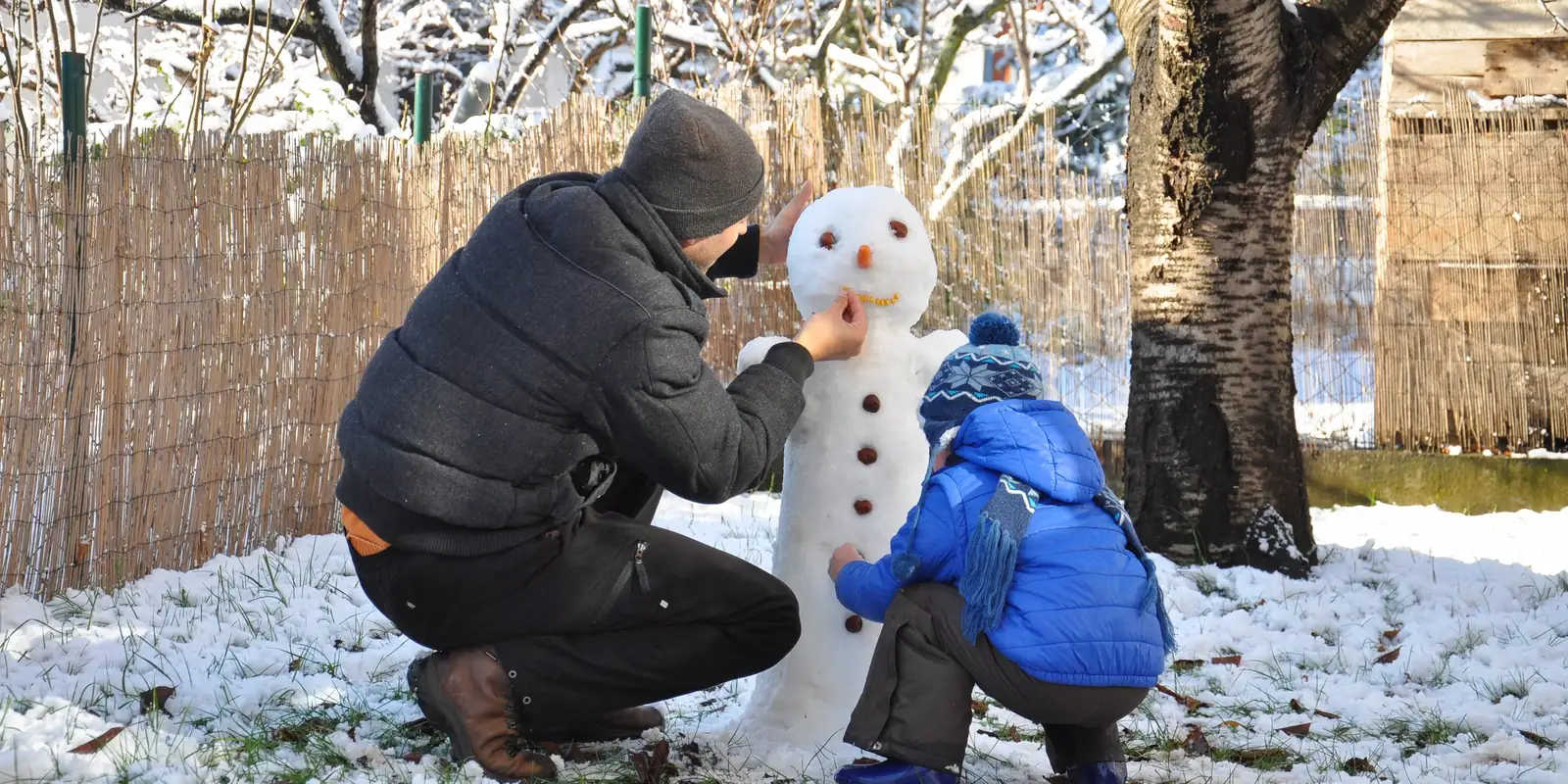 Père et enfant qui construisent un bonhomme de neige pendant des vacances à la montagne